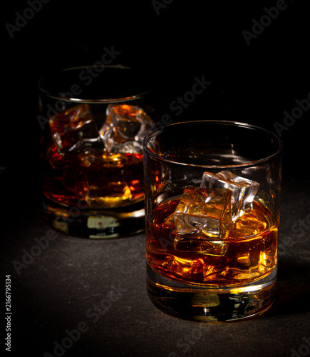 Obraz na plátne Two glasses of whiskey with ice cubes on dark slate background