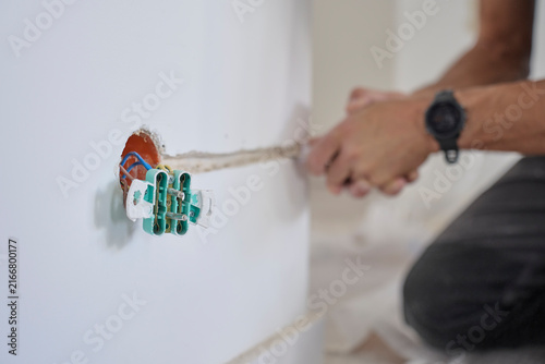 Man cuts channel in wall for electrical wire near exposed outlet