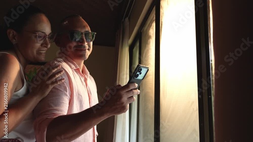 Romantic couple taking photos with smartphone near a window