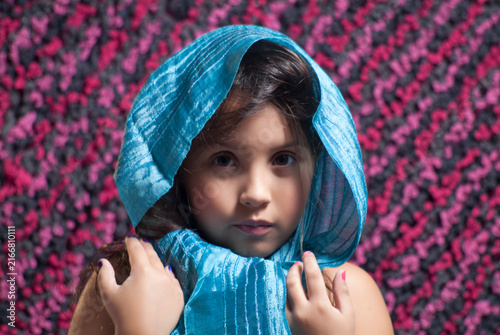 Portrait of a cute young girl wearing a bright blue headscarf looking directly at the camera