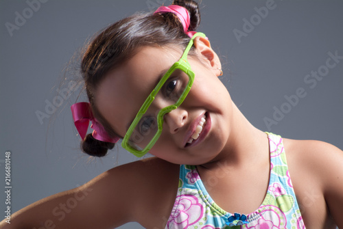 Playful young girl wearing bright green 3D glasses and pink hair bows tilting her head with a happy smile