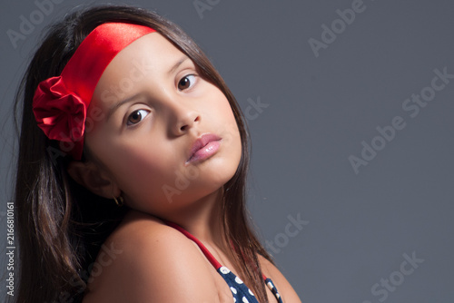 Close-up studio portrait of a young girl wearing a red floral headband gazing thoughtfully at the camera