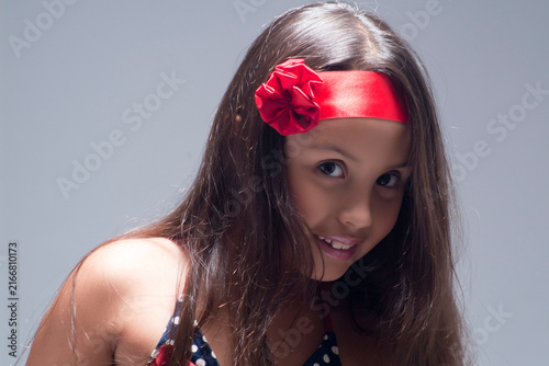 Smiling young girl with long brown hair wearing a bright red floral headband looking happily at the camera