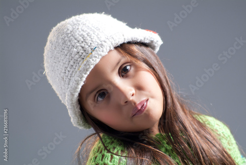 Close-up studio portrait of a sweet young girl wearing a white knitted hat and green sweater looking at the camera