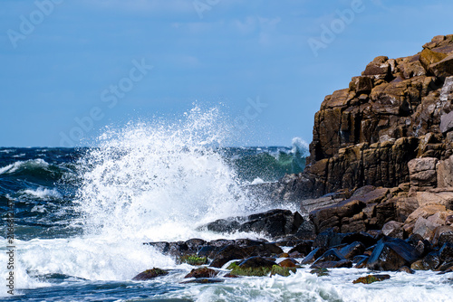 Powerful wave crashing against dark rocky coastal cliffs