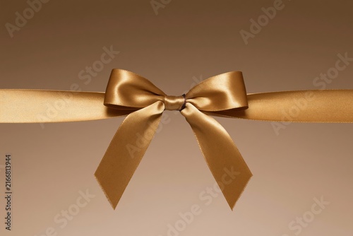 Gold satin bow and ribbon on a warm tan background, featuring soft woven textures and a luxurious sheen for festive headers and gift mockup designs