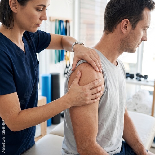 Physical therapist treating shoulder injury of a young man in clinic  