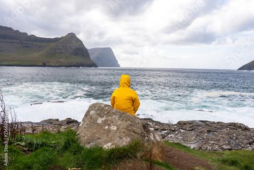 фотографія Person in yellow jacket contemplating ocean view in Faroe Islands
