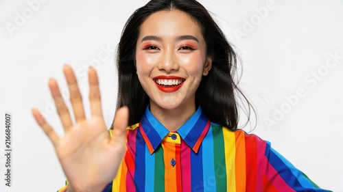 Young Woman Waving Hello: A cheerful young woman with a radiant smile and bold makeup offers a friendly wave, her colorful, striped shirt adding a vibrant touch.