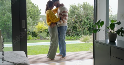 African American couple entering deck barefoot through sliding door, dancing, hugging, showing love
