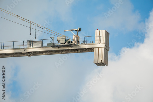 Canvastavla Heavy industrial white tower crane jib with concrete counterweights suspended high against a cloudy blue sky