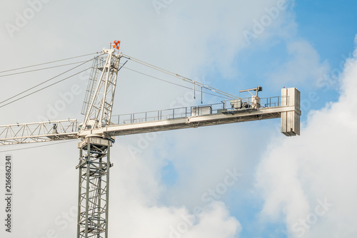 Konstfotografi Close-up of a white metal tower crane jib and counterweights operating against a cloudy blue sky on a construction site