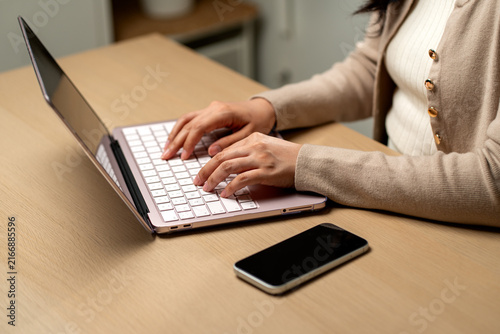 Woman typing on laptop with smartphone nearby in modern home office workspace