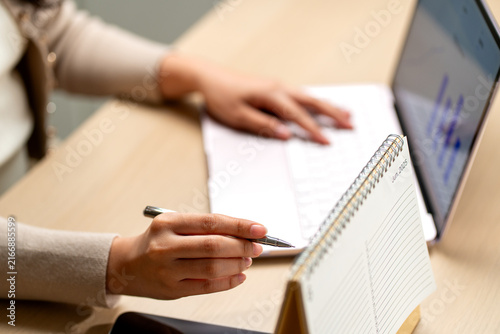Woman reviewing financial plans with pen in hand beside laptop and June 2025 calendar on wooden desk