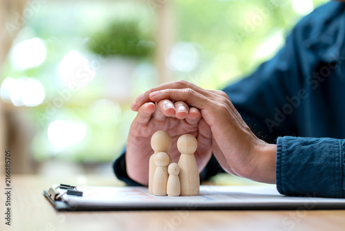 Hands gently cupping wooden family figurines over financial documents on warm wooden desk