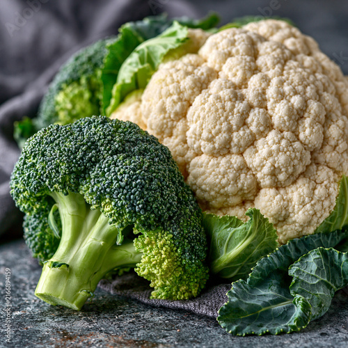 Fresh cauliflower and broccoli heads with green leaves on dark rustic background