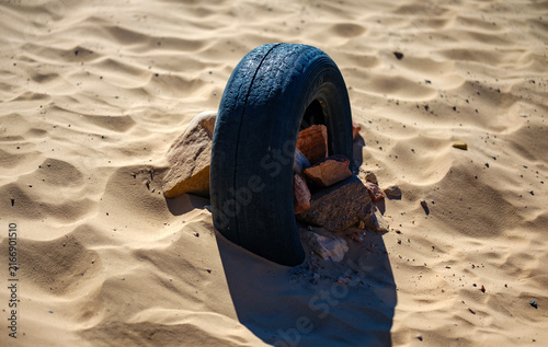 фотографія Old discarded tire embedded in sandy desert soil surrounded by rocks