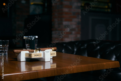 Foto smoking cigar in an ashtray and glass cognac on dark background