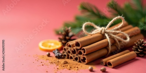 Aromatic Cinnamon Sticks Bundled with Twine, Ground Cinnamon, Dried Orange Slice, and Pine Cones on a Pink Background