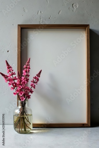 A minimalist still life featuring a simple wooden frame and a glass vase filled with delicate pink blossoms, subtly illuminating a calm and serene atmosphere.