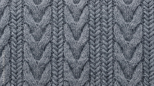 Detailed close up of a gray cable knit sweater texture showing interwoven yarn patterns with soft studio lighting