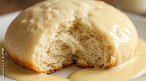 Soft and fluffy freshly baked dinner roll covered in thick creamy sauce on a white plate