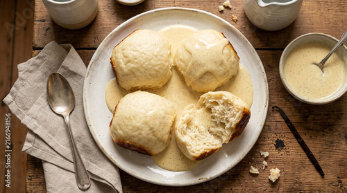 Traditional German yeast dumplings served with warm vanilla sauce on a rustic wooden table