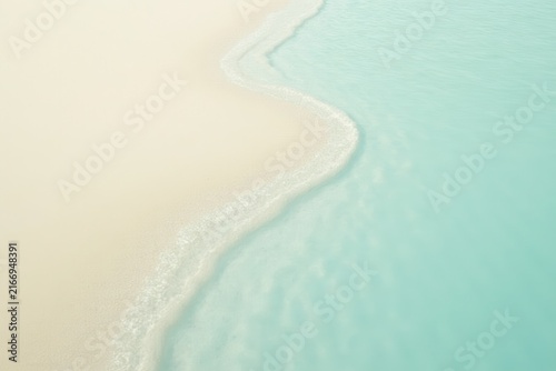 Smooth sandy beach meeting clear turquoise water, with gentle waves lapping at the shore and soft curves along the coastline, evoking serene tranquility and natural beauty.
