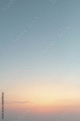 Pastel sky fading from warm orange and pink near the horizon into soft blue above, with faint wispy clouds scattered, capturing serene beauty of sunrise or sunset.