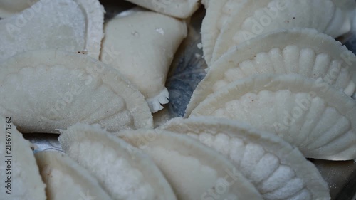 Close-up of raw homemade dumplings arranged on a tray, showing white dough folded edges and food preparation texture