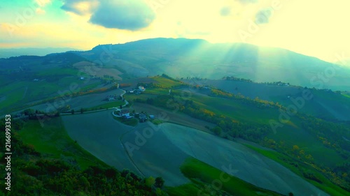 Glorious aerial pullback shot from near Santa Vittoria in Matenano, the stunning light of the sun piercing through the clouds and the Sibillini Mountains, imbuing the sky with golden immortal quality