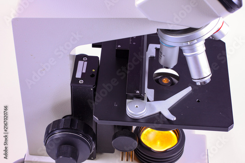 Detailed view of a classic scientific microscope featuring a rotating objective turret, interchangeable lenses, glass slide holder and adjustable mechanical stage for microscopic examination.