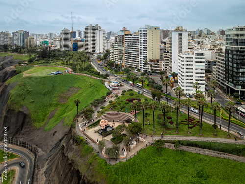 Aerial view of Love Park with its iconic sculpture, lush green gardens, and palm trees situated on the dramatic coastal cliffs of Miraflores, Peru