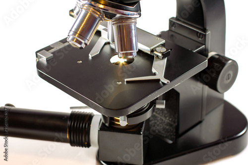 Close-up of a laboratory microscope with objective lenses, mechanical stage, specimen holder and illuminated condenser for scientific research and microscopic observation.