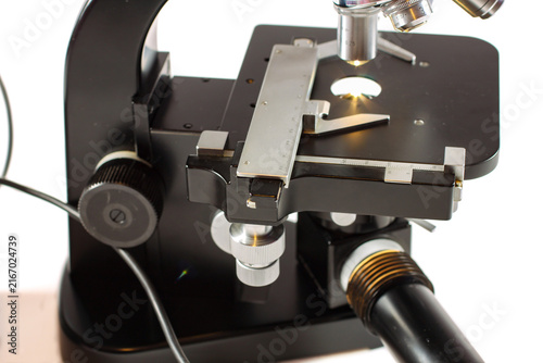 Detailed view of a precision microscope featuring multiple objectives, adjustable stage, specimen holder and focused illumination on a clean white background.