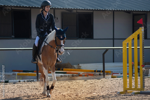 teenage girl in riding attire waits on her horse, anticipating being called to participate in the show jumping competition on the track.