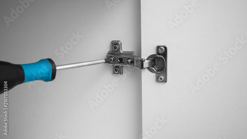 Photography Screwdriver working on cabinet hinge in a home repair setting