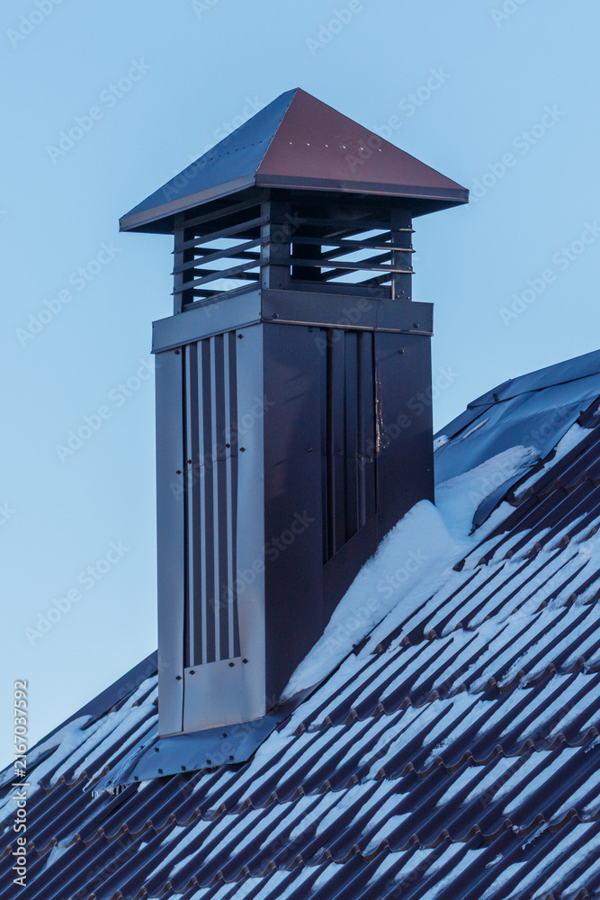 Fototapeta premium Snow covers roof tiles beneath a chimney with red-topped vent