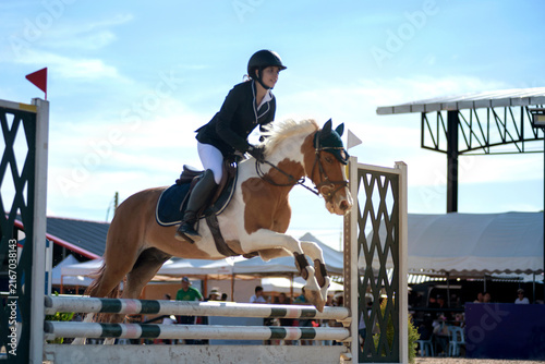 Teenage equestrian girl in her competition attire is participating in show jumping on the course.