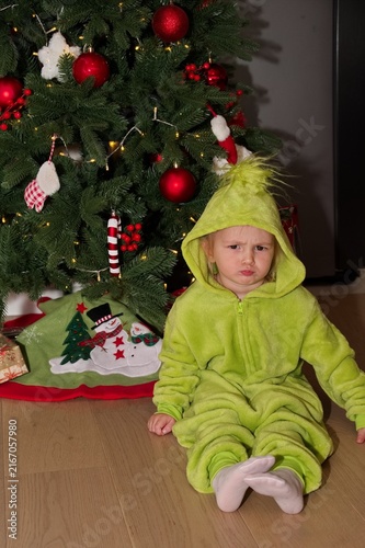 Cute little girl in costume sitting in front of Christmas tree