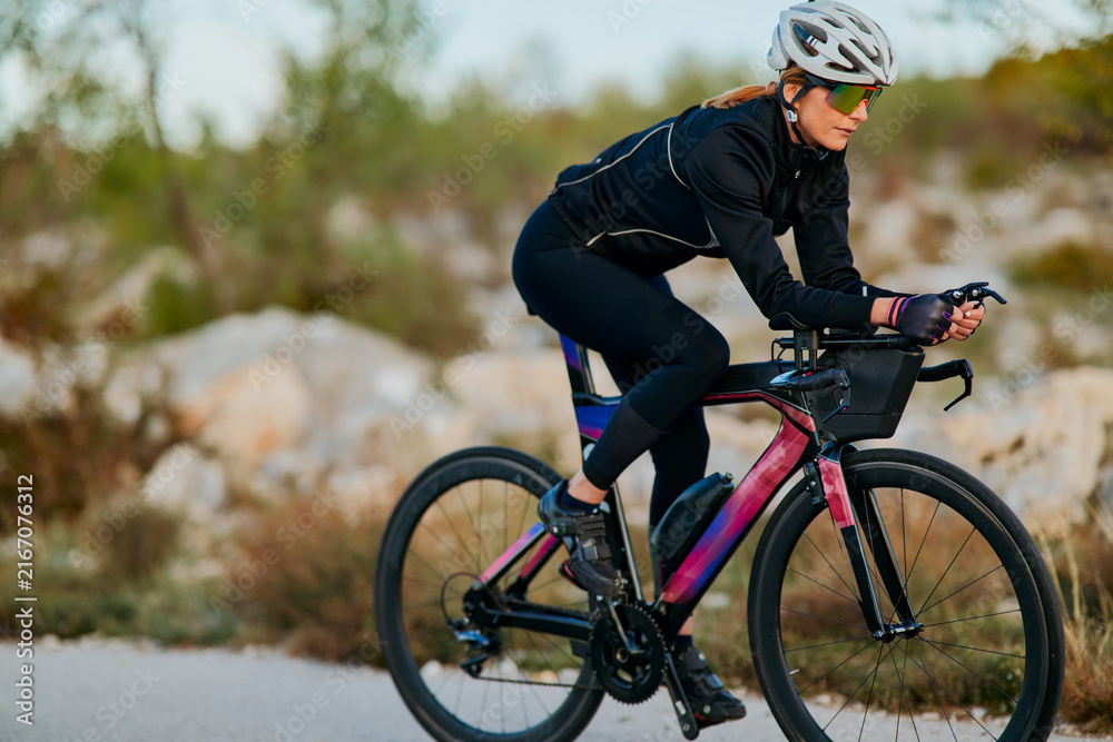 Fototapeta premium Female Cyclist Riding Aerodynamic Road Bike on Rural Road Training for Triathlon Time Trial