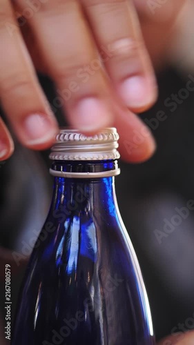 Hand opening a blue glass bottle