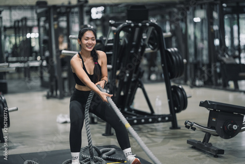 Woman exercising with battle ropes or training sled pull in gym