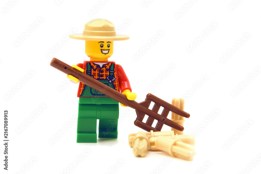 Fototapeta premium Lego minifigure of happy farmer with pitchfork or hayfork is doing isolated on white. Editorial illustrative image of popular plastic toy.