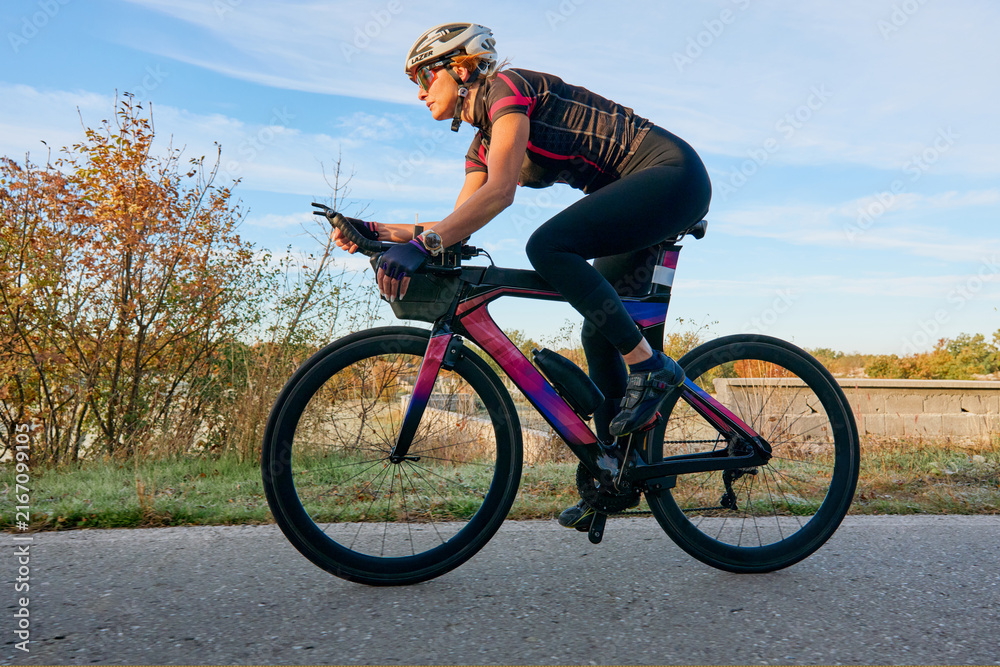 Fototapeta premium Female Cyclist Riding Road Bike In Aerodynamic Position On Countryside Pavement At Sunrise