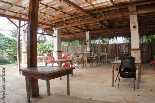 Fotografie Wooden tables and mismatched chairs stand beneath a rustic roof in a quiet local restaurant area