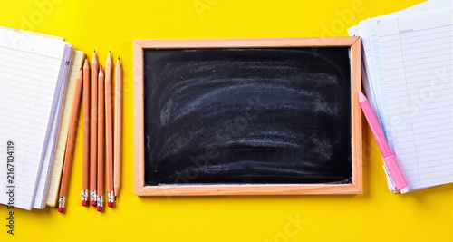 Flat lay composition with school supplies : chalkboard, pencils, and notebooks on yellow desk
