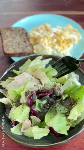 close-up vertical shot of a fresh green salad being tossed with a black fork in a dark bowl