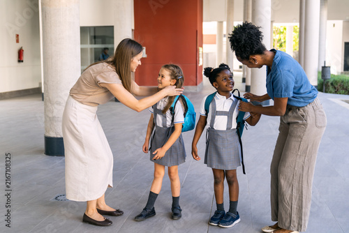 Multiethnic mothers helping young girls adjusting backpacks before entering school, celebrating diversity and education journey