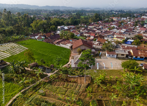 Foto Aerial View of Rice Fields Adjacent to a Rural Settlement with Green Hills in the Distance